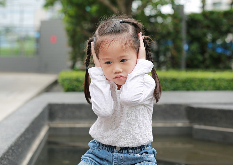 Little girl with braided pigtails covering her ears