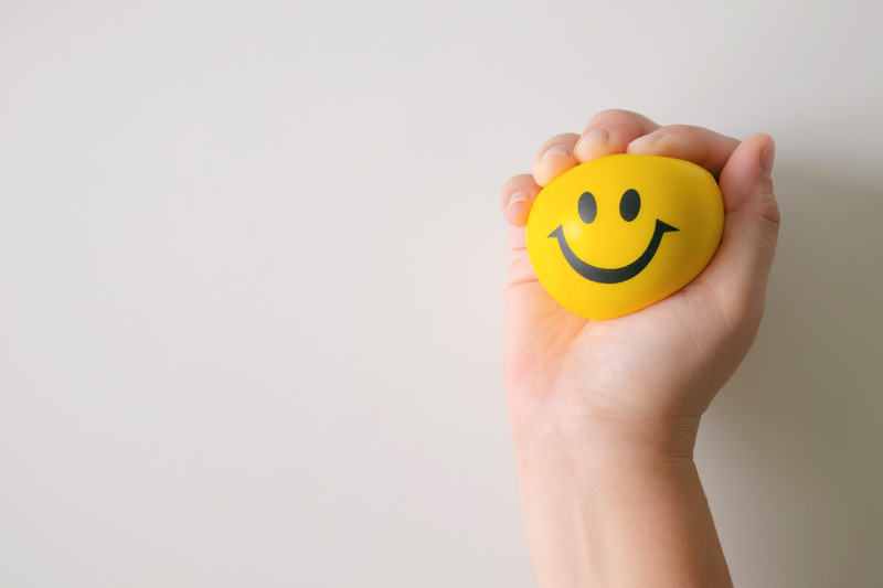 A hand squeezing a yellow ball with a smiley face