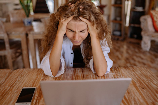 Frustrated woman sitting with her head in her hands, a computer in front of her.