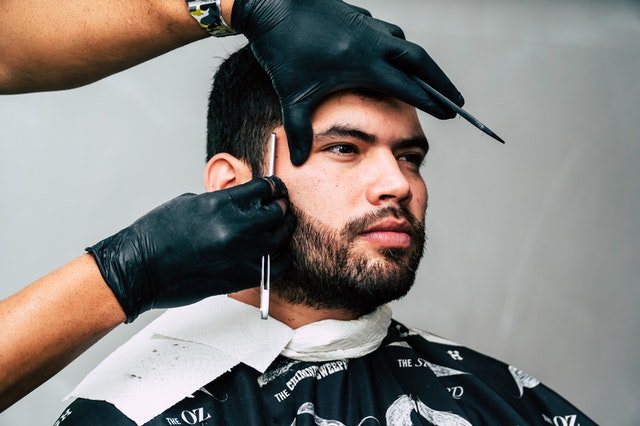 Young man with a beard getting a professional haircut and shave.