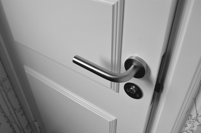 A white door with a silver knob and lock opened a crack.