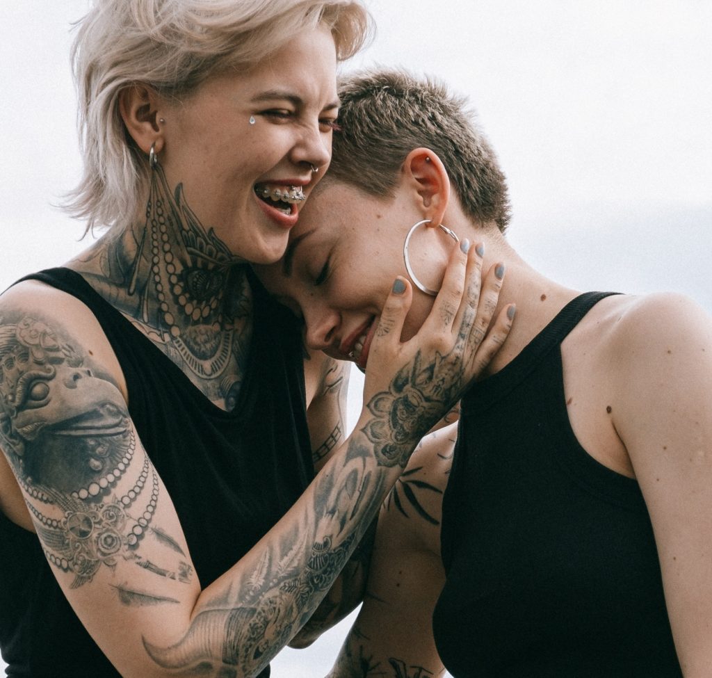 Two young women with tattoos embracing and laughing.