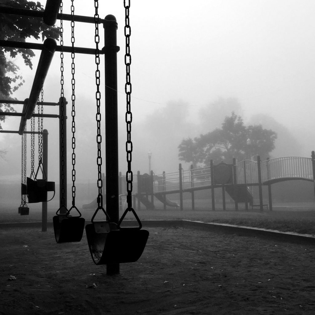 Black and white photo of a swing set and playscape looking creepy and lonely.