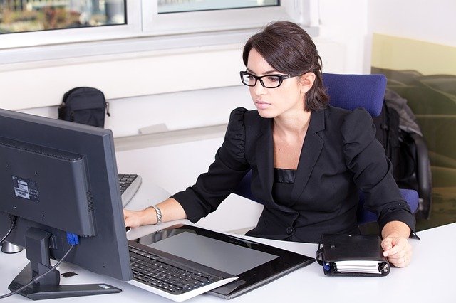 An attractive young woman with brown hair and glasses looking intently at a computer screen.