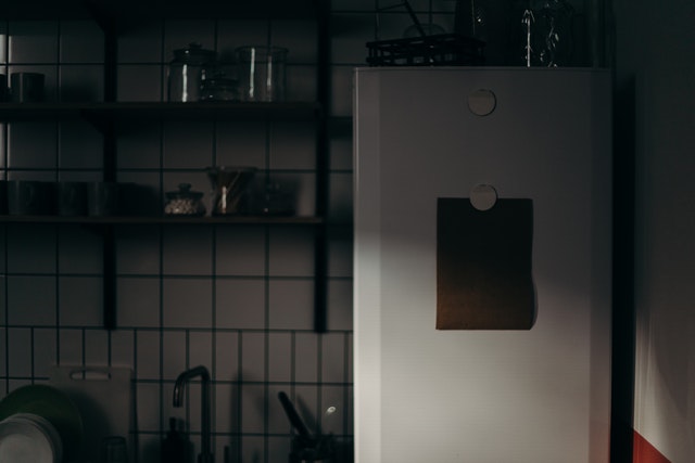 Side view of a white fridge in a dark kitchen setting.