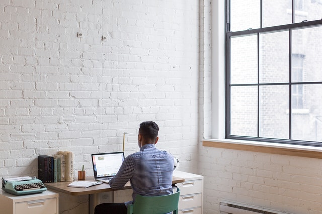 Man at a desk working on a computer with his back to a wall.