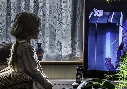 Little girl with long hair in a ponytail watching TV.