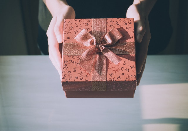 Close-up photo of a person holding a pink gift box with a bow.