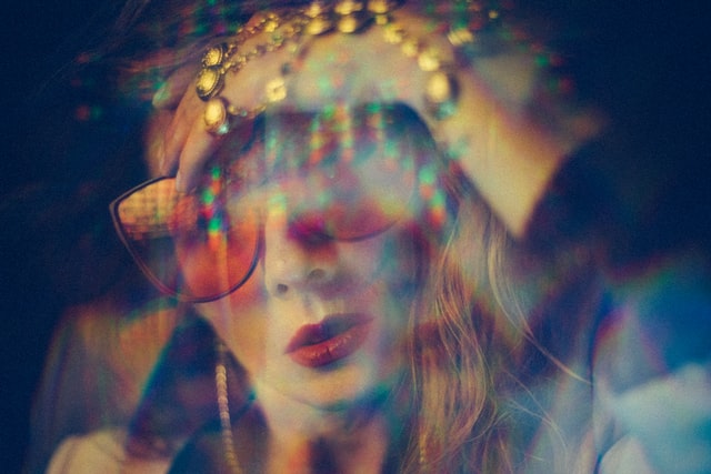 An experimental, slightly blurred photo of a woman with sunglasses and red lipstick with her hand on her head. 