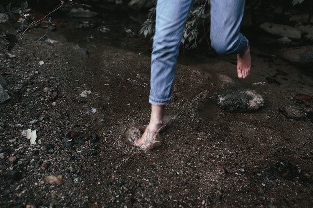 A close-up photo of legs in a pair of jeans with bare feet running into water.