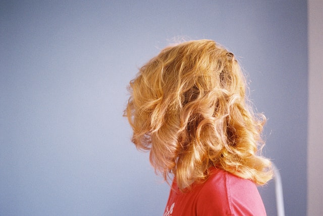 A person with strawberry blonde hair showing the back of her head. Person is wearing a pink shirt and has their face turned from the camera. 
