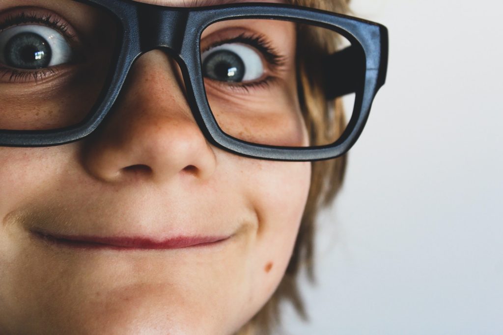 Cute child with large, dark glasses, smiling at the camera.