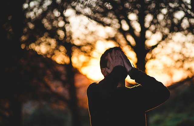 Man with his hands over his face with a sunset in the background. 