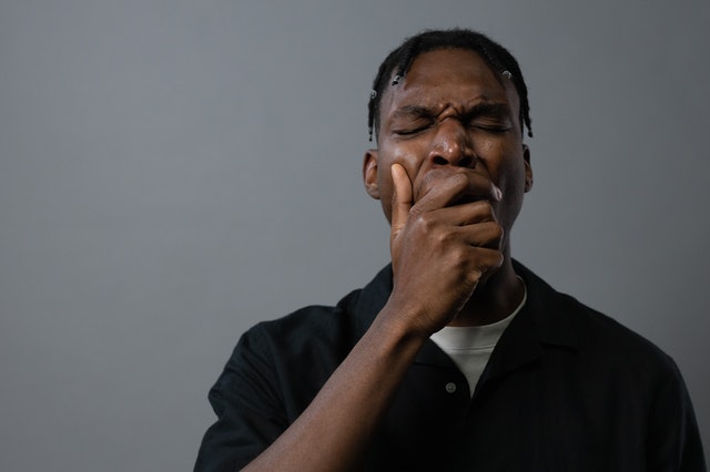 African American man wearing a black button-down shirt yawning and covering his mouth.