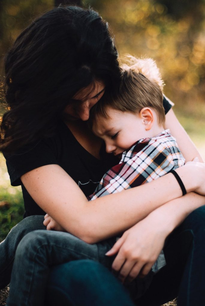 A mother holding her son, who looks upset.