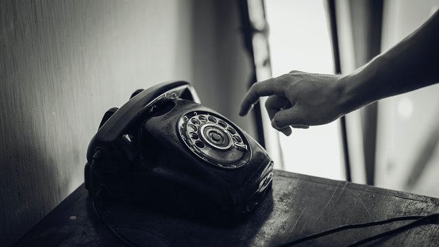 Black and white photo of a person's hand reaching for an old-fashioned rotary phone.