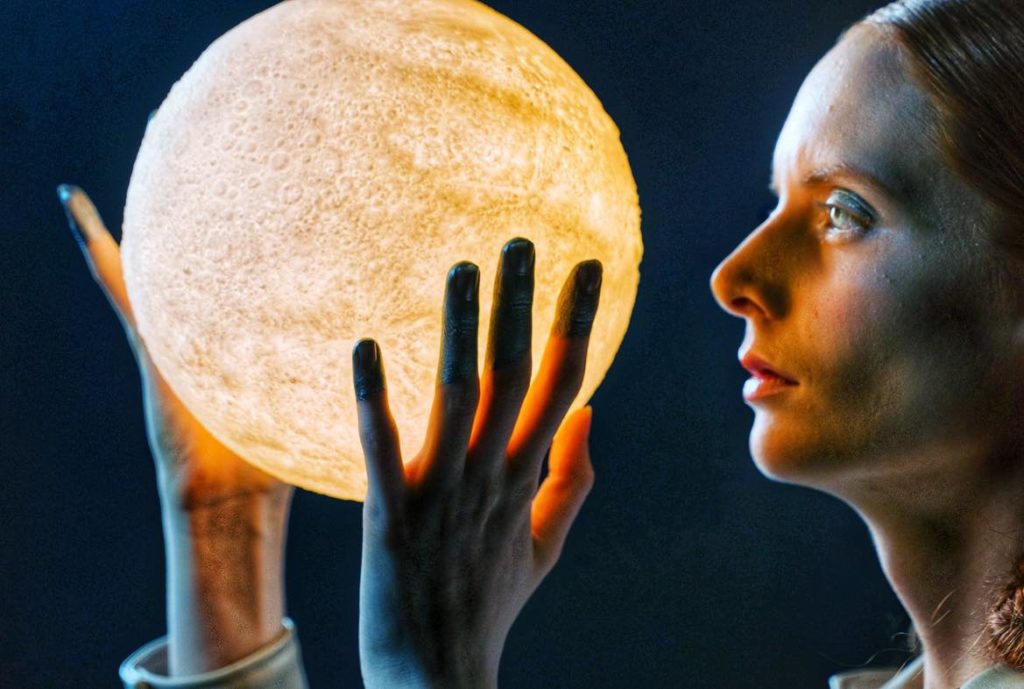 Woman gazing intently at a light-up ball in the shape of a moon.