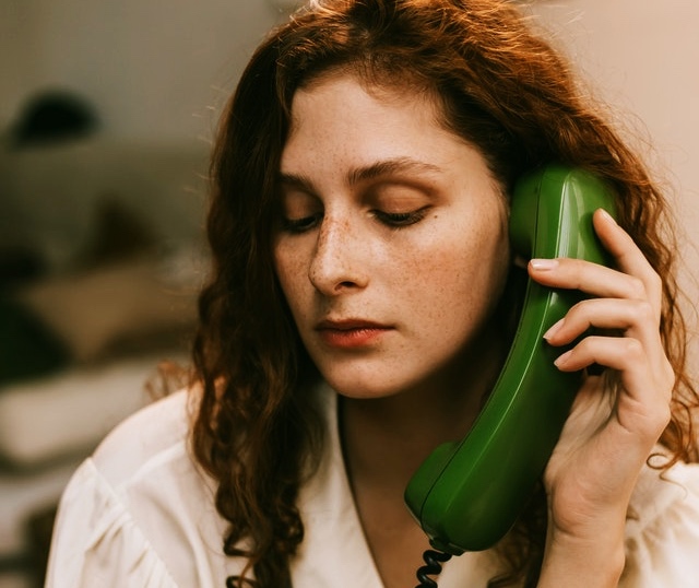 Redheaded woman with freckles holding a green phone to her ear. 