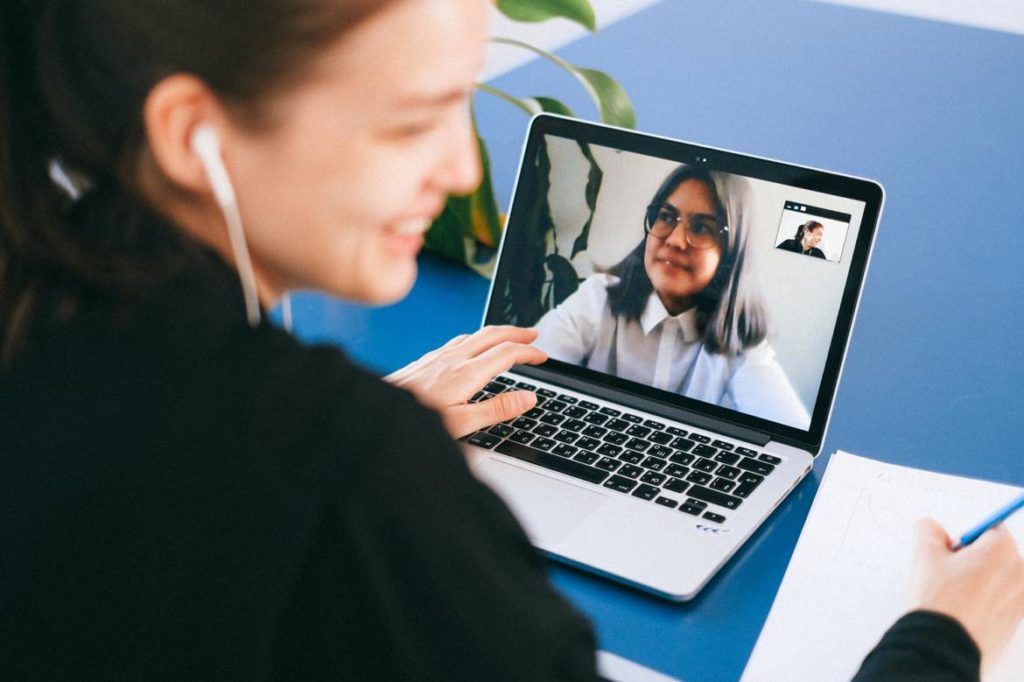Two female-presenting people on a video call. One wears corded earbuds, the other wears glasses. 
