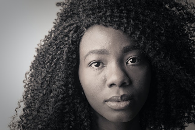 Young woman with soulful brown eyes and curly, dark hair stares intently into the camera. 