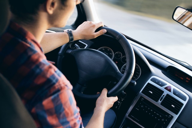 Close-up image of a person driving a car. Their hands are on the wheel, and the road before them is blurred. 