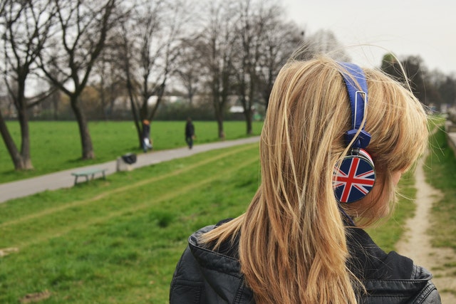 Young blonde girl with headphones on her ears. Her back is turned to the camera. 