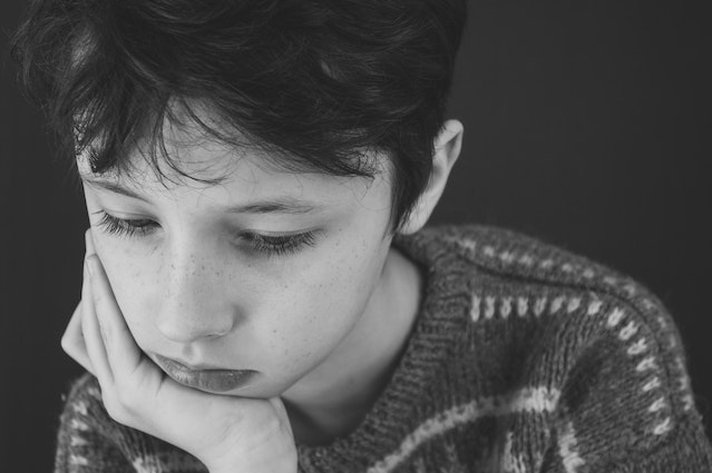 A black and white photo of a young boy resting his head on his chin. He looks sad and/or defeated. 