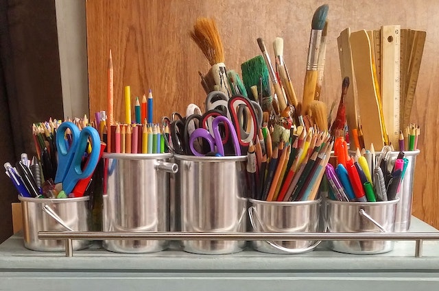 A bunch of art supplies in silver buckets. Paintbrushes, colored pencils, rulers, scissors, markers, etc. 