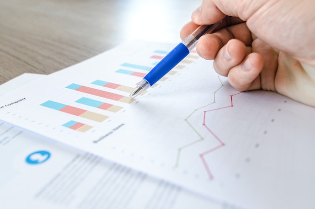 A closeup photo of a hand holding a blue pen working on a graph of data. 