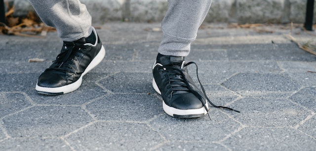 A closeup photo of a person wearing black and white sneakers; their left shoe is untied. 