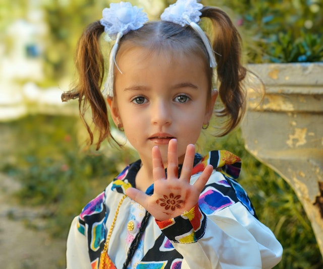 Beautiful little girl with pigtails holding her hand out with a design on it. 
